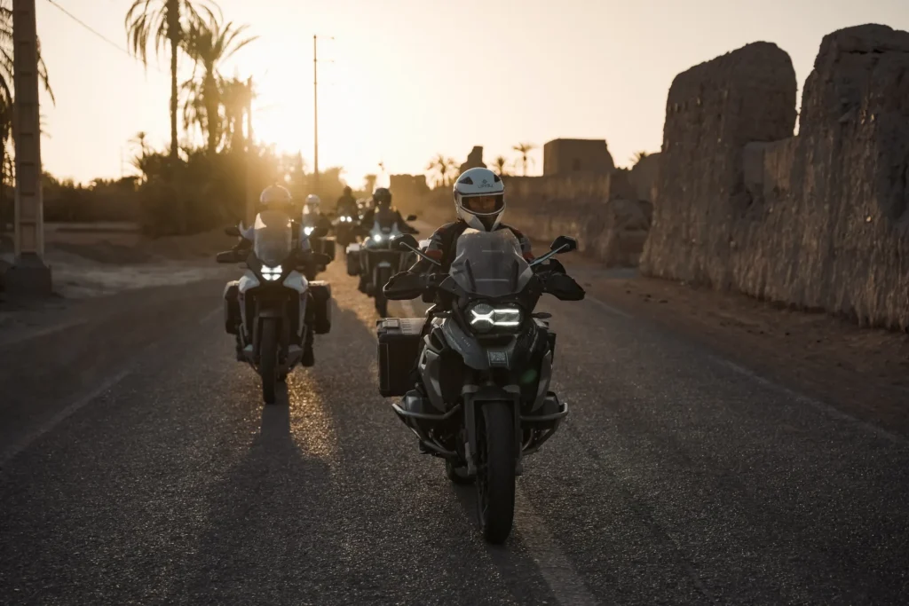 Pilotos en motos BMW al atardecer junto a una muralla de adobe